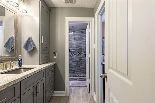 bathroom with tiled shower, vanity, a textured ceiling, and hardwood / wood-style flooring