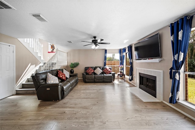 living room featuring a tiled fireplace, ceiling fan, a textured ceiling, and light wood-type flooring