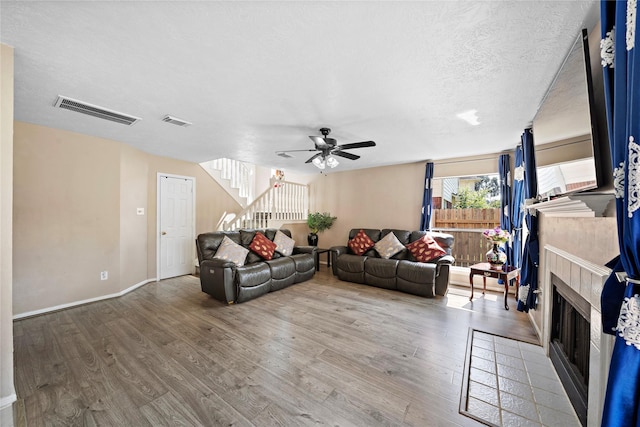 living room featuring ceiling fan, wood-type flooring, a textured ceiling, and a tile fireplace