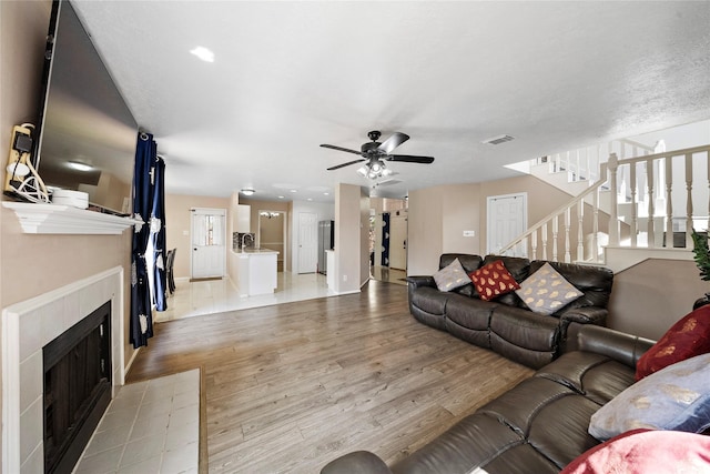 living room featuring a tile fireplace, light hardwood / wood-style floors, ceiling fan, and sink