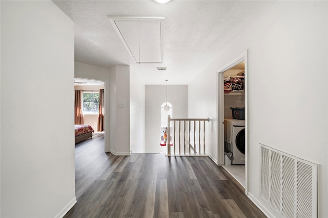 corridor with a textured ceiling, washer / clothes dryer, and dark hardwood / wood-style floors