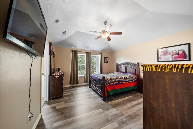 bedroom with a textured ceiling, hardwood / wood-style flooring, ceiling fan, and lofted ceiling