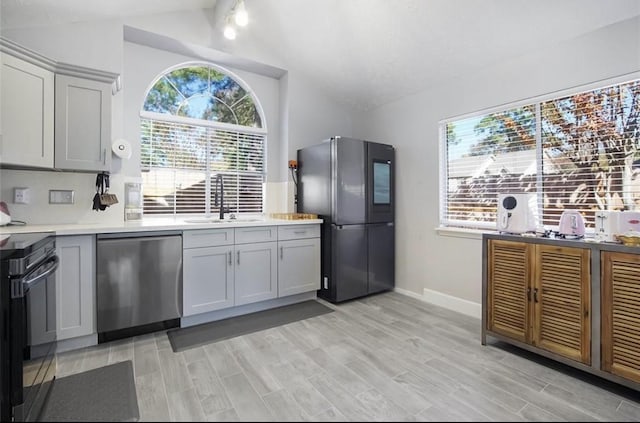 kitchen featuring gray cabinetry, sink, light hardwood / wood-style flooring, vaulted ceiling, and appliances with stainless steel finishes