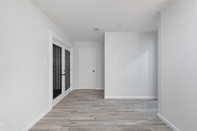 hallway featuring french doors, a textured ceiling, and light hardwood / wood-style flooring