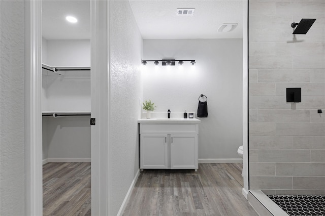 bathroom with vanity, toilet, wood-type flooring, and tiled shower