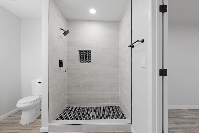 bathroom with tiled shower, wood-type flooring, and toilet