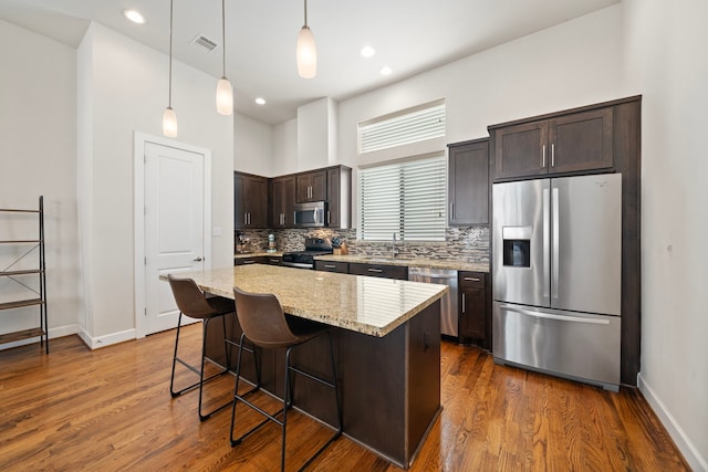 kitchen with hanging light fixtures, a kitchen bar, dark brown cabinets, a kitchen island, and appliances with stainless steel finishes