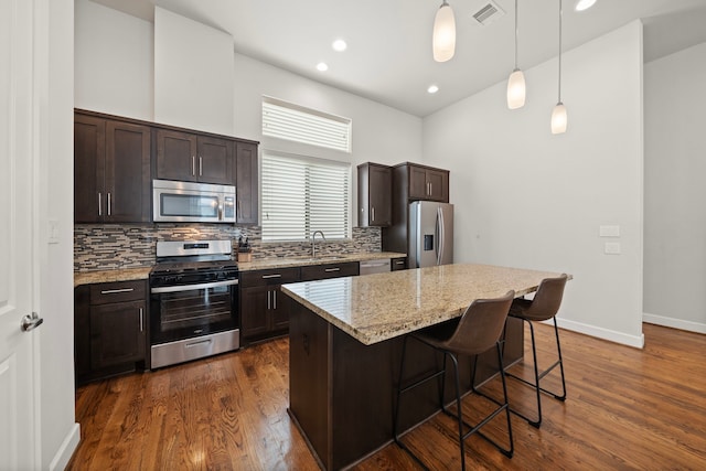 kitchen featuring sink, stainless steel appliances, decorative light fixtures, a breakfast bar area, and a kitchen island