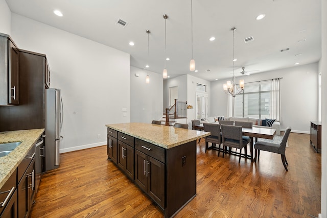 kitchen featuring light stone countertops, stainless steel fridge, dark brown cabinetry, pendant lighting, and a kitchen island