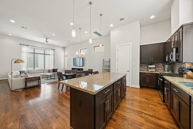 kitchen with appliances with stainless steel finishes, light stone counters, ceiling fan with notable chandelier, pendant lighting, and a kitchen island