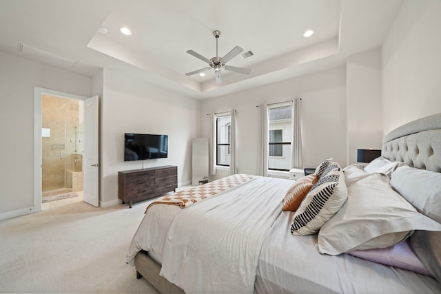 bedroom with light carpet, connected bathroom, a tray ceiling, and ceiling fan