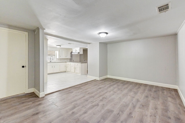 unfurnished living room with sink, a textured ceiling, and light wood-type flooring