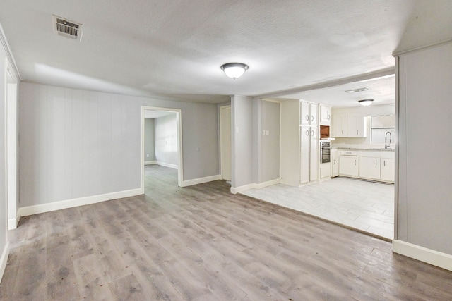 unfurnished living room featuring a textured ceiling, sink, and light hardwood / wood-style flooring