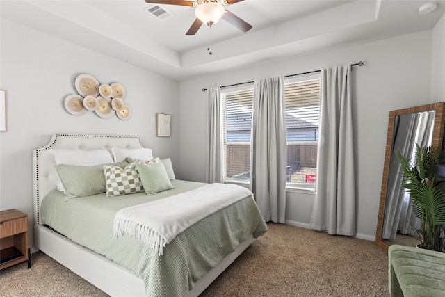 bedroom with visible vents, baseboards, ceiling fan, light colored carpet, and a tray ceiling