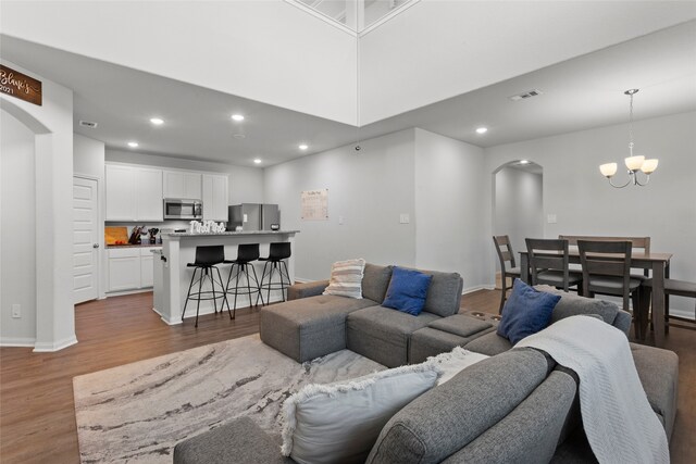 living room with an inviting chandelier, a towering ceiling, and light hardwood / wood-style flooring