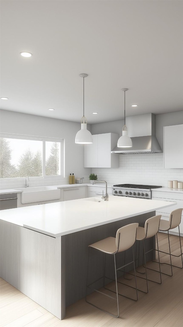 kitchen featuring white cabinets, wall chimney exhaust hood, pendant lighting, and a center island with sink