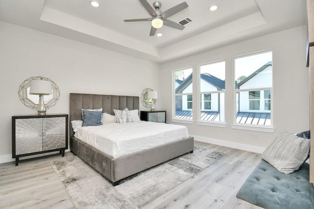 bedroom featuring ceiling fan, light wood-type flooring, and a tray ceiling