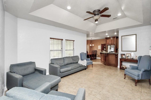 tiled living room featuring a tray ceiling and ceiling fan with notable chandelier