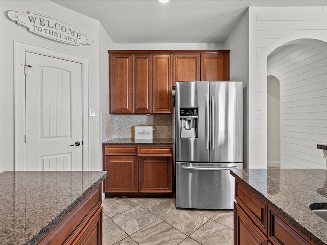 kitchen featuring tasteful backsplash, dark stone counters, stainless steel fridge, and a textured ceiling