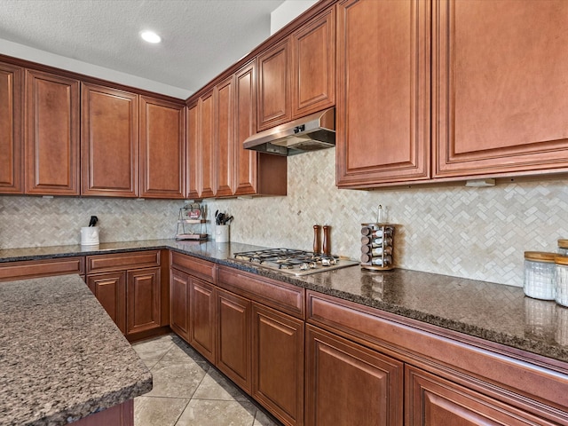 kitchen featuring tasteful backsplash, stainless steel gas stovetop, dark stone countertops, and light tile patterned floors