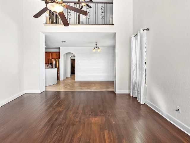 unfurnished living room with dark hardwood / wood-style flooring, a towering ceiling, and ceiling fan