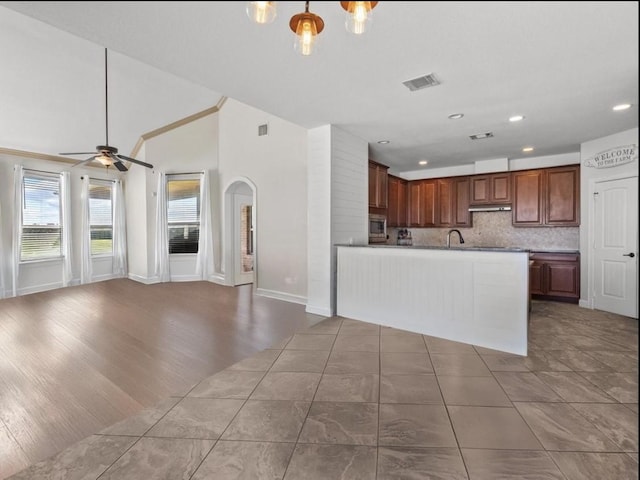 kitchen featuring lofted ceiling, ceiling fan, hardwood / wood-style floors, stainless steel microwave, and decorative backsplash