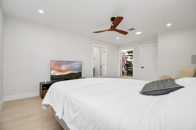 bedroom with a walk in closet, a closet, light hardwood / wood-style flooring, and ceiling fan