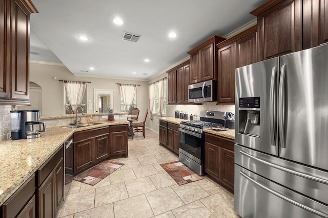 kitchen with appliances with stainless steel finishes, backsplash, light stone counters, ornamental molding, and sink