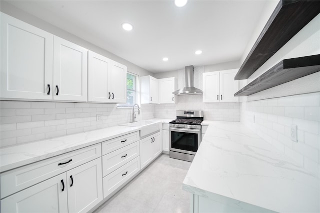 kitchen with wall chimney exhaust hood, white cabinetry, sink, and stainless steel range with gas stovetop