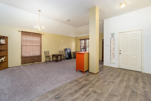 interior space with kitchen peninsula, vaulted ceiling, decorative light fixtures, a notable chandelier, and hardwood / wood-style floors