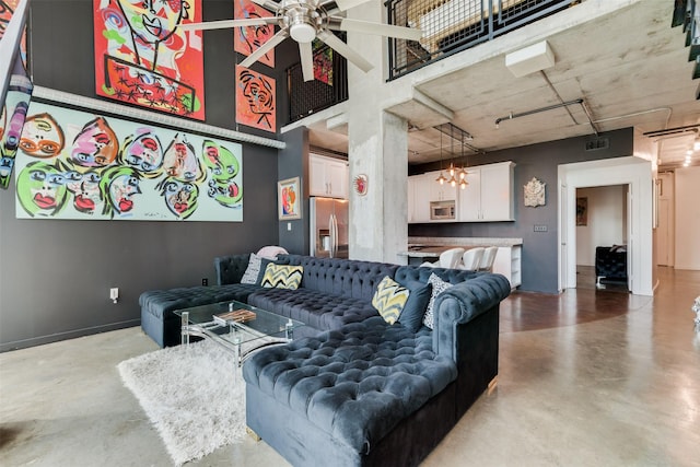 living room featuring a towering ceiling, concrete flooring, and ceiling fan with notable chandelier