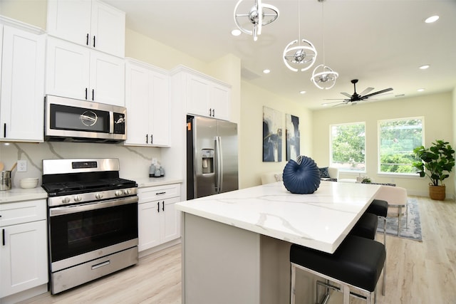 kitchen featuring white cabinetry, stainless steel appliances, a kitchen breakfast bar, decorative light fixtures, and a kitchen island