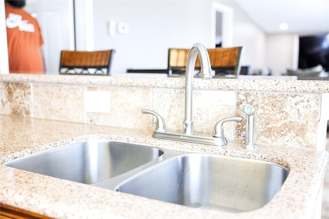 interior details featuring decorative backsplash, light stone countertops, and sink