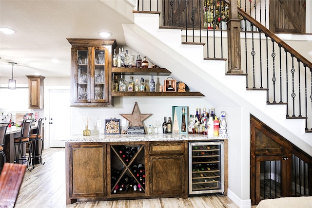 bar featuring light stone countertops, decorative light fixtures, light hardwood / wood-style flooring, and wine cooler