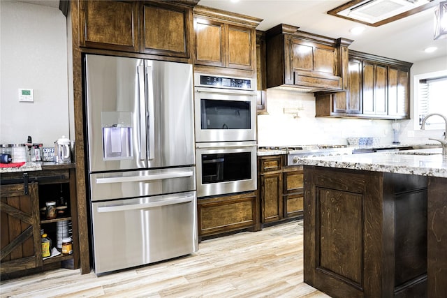 kitchen featuring appliances with stainless steel finishes, light stone counters, dark brown cabinets, sink, and light hardwood / wood-style flooring