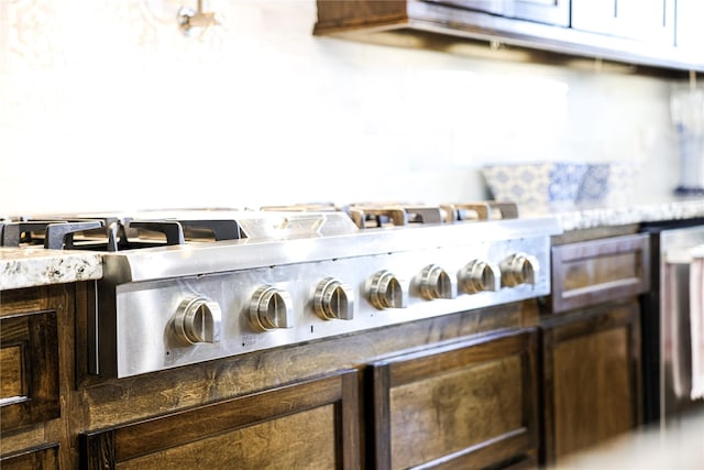 room details with stainless steel gas stovetop, light stone counters, and dark brown cabinetry