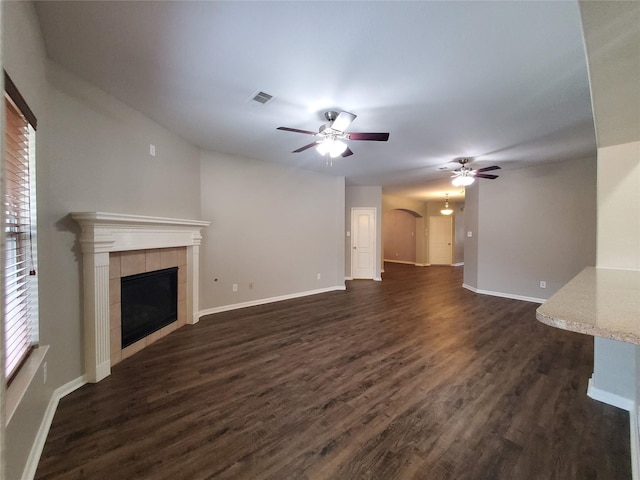 unfurnished living room with ceiling fan, dark hardwood / wood-style flooring, and a tiled fireplace