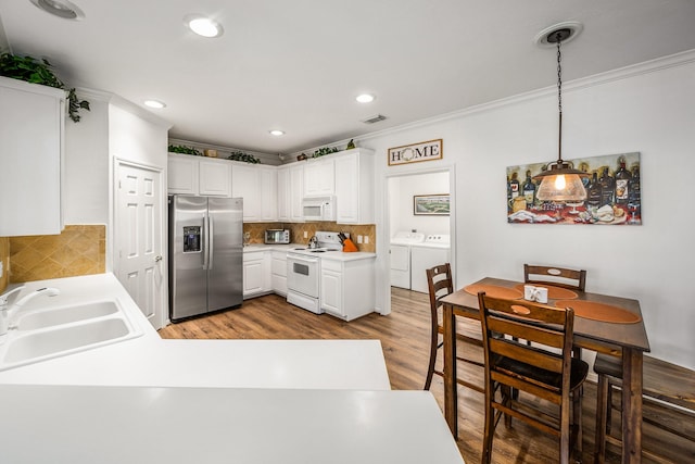 kitchen featuring white appliances, sink, hanging light fixtures, separate washer and dryer, and white cabinetry