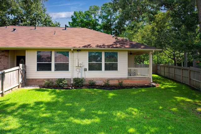 rear view of property with ceiling fan and a yard