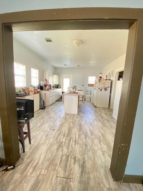 kitchen featuring a center island, light wood-type flooring, plenty of natural light, white fridge, and white cabinetry