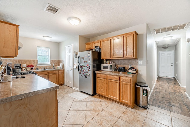 kitchen featuring stainless steel fridge, light tile patterned floors, a textured ceiling, and tasteful backsplash