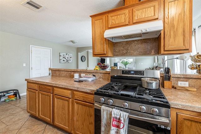 kitchen featuring light tile patterned floors, a textured ceiling, and stainless steel gas range oven