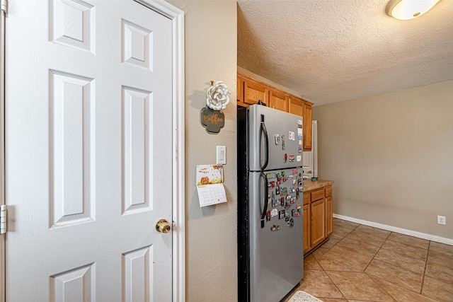 kitchen with stainless steel fridge, a textured ceiling, and light tile patterned floors