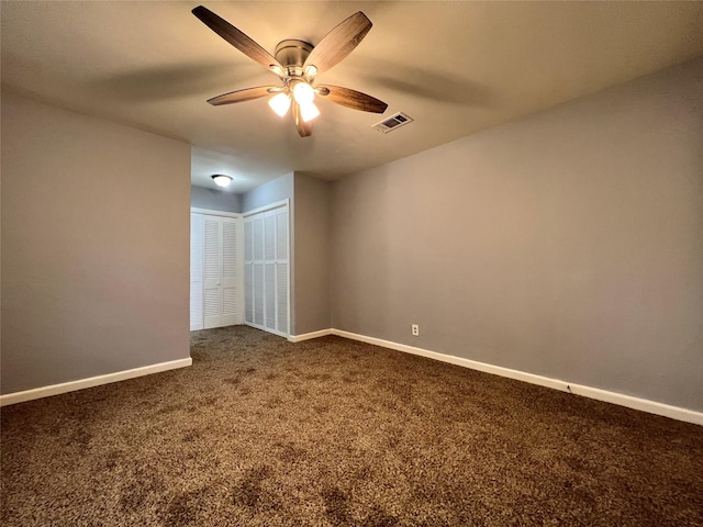 unfurnished room featuring visible vents, dark carpet, baseboards, and ceiling fan