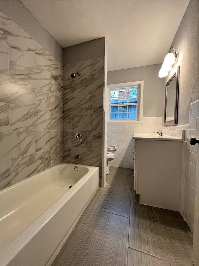 bathroom with vanity, wainscoting, tile walls, toilet, and shower / bathtub combination