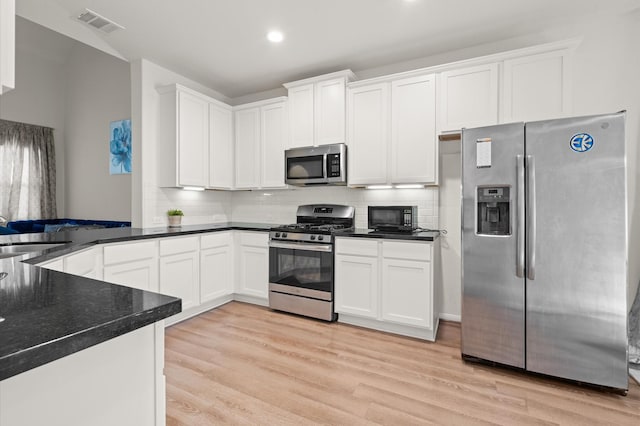 kitchen featuring appliances with stainless steel finishes, white cabinetry, decorative backsplash, sink, and light hardwood / wood-style flooring