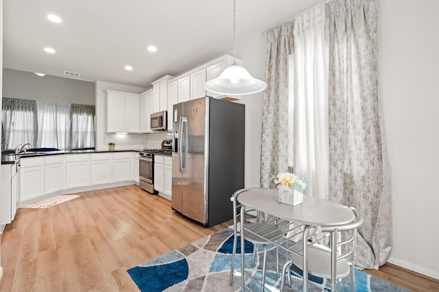 kitchen with white cabinets, appliances with stainless steel finishes, decorative light fixtures, decorative backsplash, and light hardwood / wood-style floors