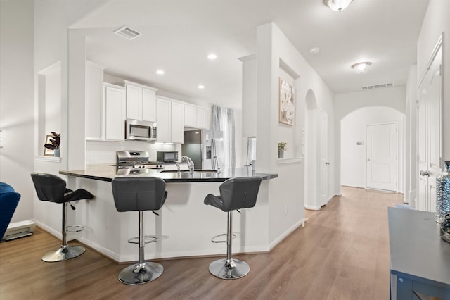 kitchen featuring white cabinets, stainless steel appliances, kitchen peninsula, light hardwood / wood-style flooring, and a breakfast bar area