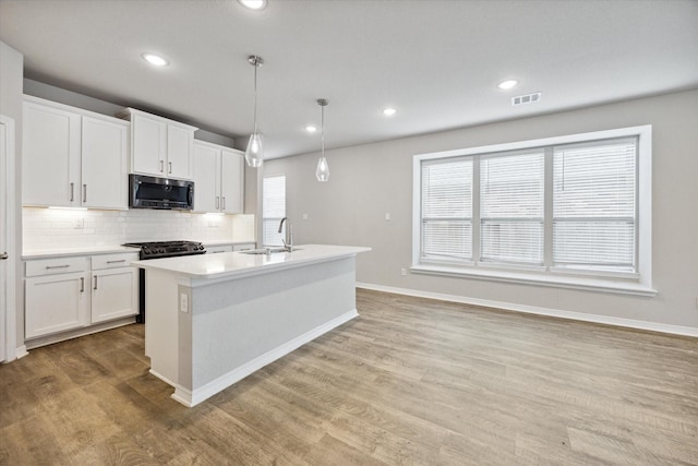 kitchen featuring a kitchen island with sink, white cabinetry, light hardwood / wood-style flooring, and hanging light fixtures