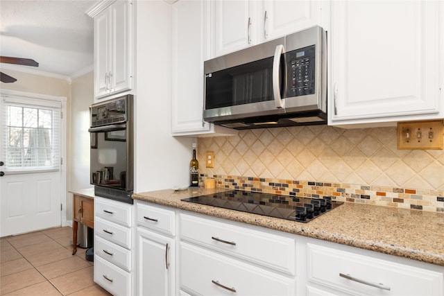 kitchen with backsplash, light stone counters, black appliances, light tile patterned floors, and white cabinetry